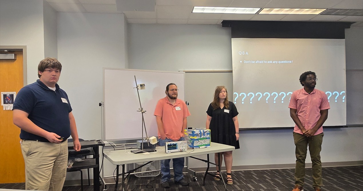 four students looking out into the audience as their presentation shows Q and A, Don't be afraid to ask any questions