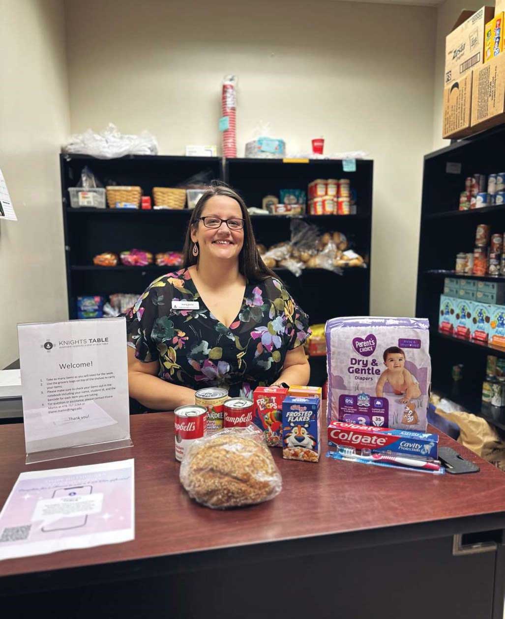Elaine Martin smiling, seated at a desk with pantry shelves and items surrounding her