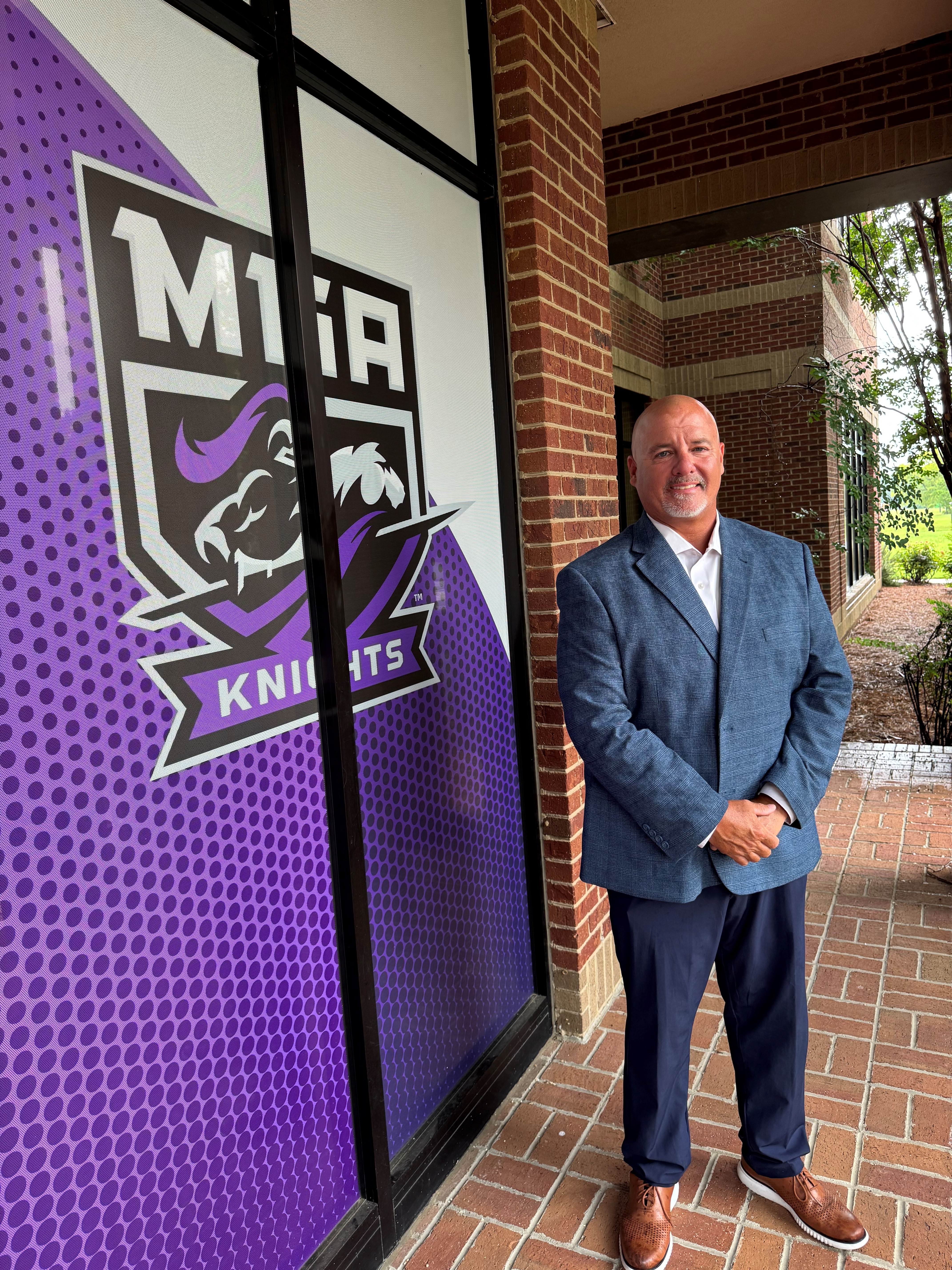 Dr. Doug Rizer poses in front of MGA Knight Logo