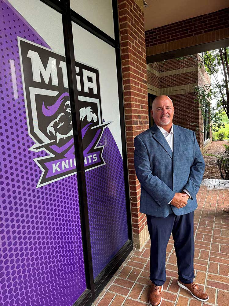 Dr. Doug Rizer poses in front of MGA Knight Logo