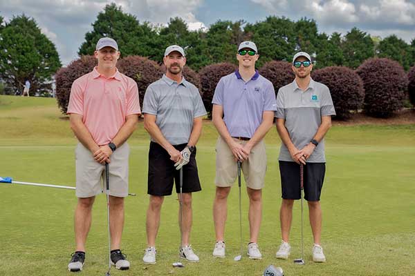 Four men holding their golf clubs on a field